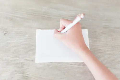 Hand holding a pen over a blank piece of paper on a light wooden surface