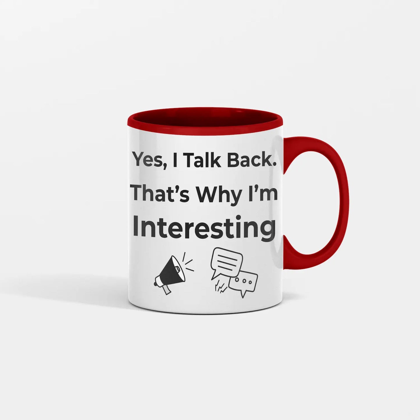 White ceramic coffee mug with bold black text reading “Yes I Talk Back. That’s Why I’m Interesting,” on a kitchen table with coffee steam rising.