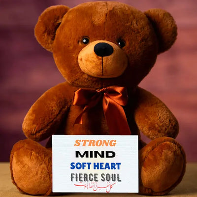 Brown teddy bear with a sign that reads 'Strong mind, soft heart, fierce soul' on a blurred background.