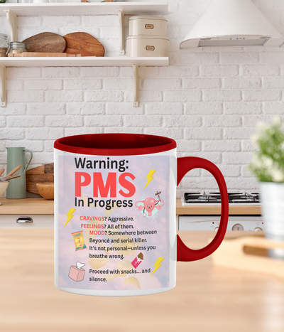 White ceramic coffee mug with bold text reading “PMS IN PROGRESS – Proceed at Your Own Risk” in a fun, comic-style font – perfect for women’s humor gifts.