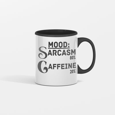 White ceramic coffee mug reading “Mood: Sarcasm 80% Caffeine 20%” in bold black lettering, sitting on a wooden desk beside a laptop and notebook.