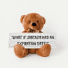 A teddy bear sitting on a wooden surface holding a sign with the phrase 'WHAT IF SARCASM HAD AN EXPIRATION DATE?'