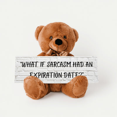 A teddy bear sitting on a wooden surface holding a sign with the phrase 'WHAT IF SARCASM HAD AN EXPIRATION DATE?'