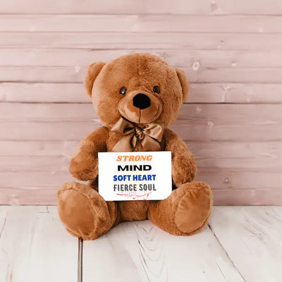 Brown teddy bear holding a sign with motivational text against a wooden background
