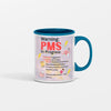 White ceramic coffee mug with bold text reading “PMS IN PROGRESS – Proceed at Your Own Risk” in a fun, comic-style font – perfect for women’s humor gifts.

