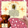 A soft plush teddy bear holding a heart-shaped tag and a printed card titled “To My Wife – Never Forget.” Set on a white gift box surrounded by roses and ribbon.