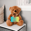 "Plush teddy bear holding a card with the message 'Mom, We Love You – Forever Our Guide' on a pink floral background."