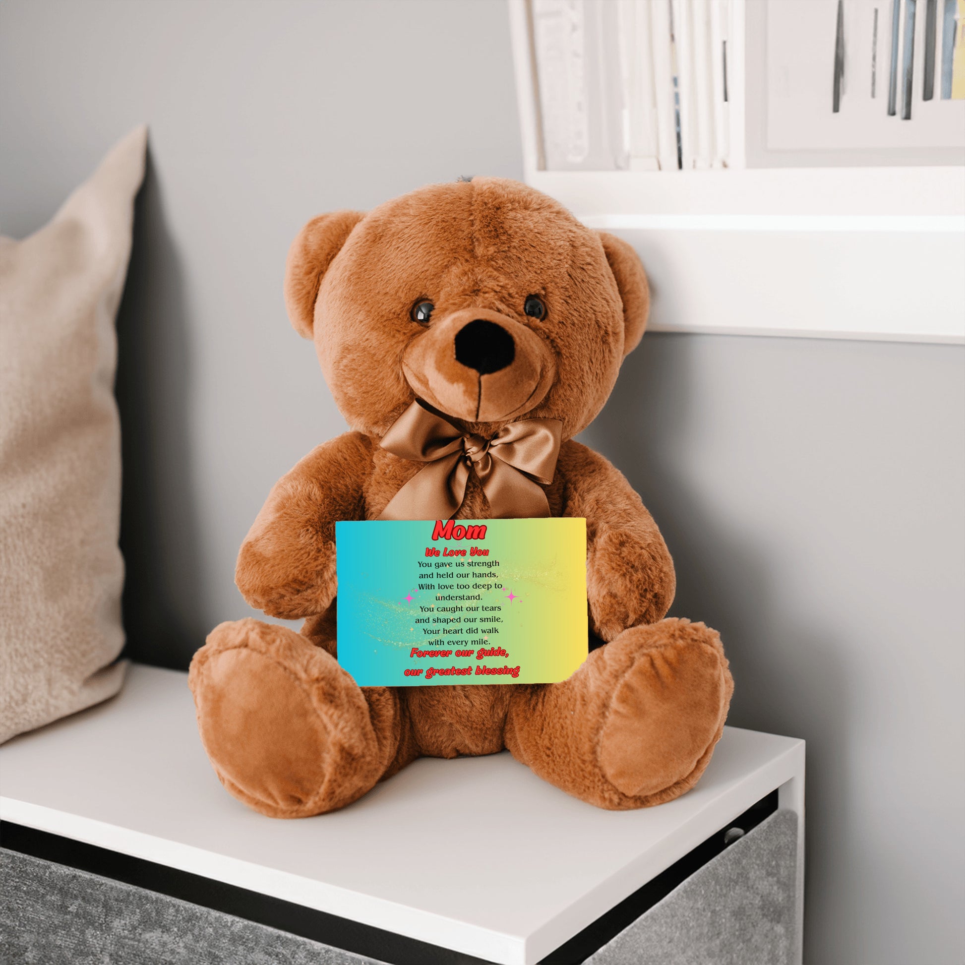 "Plush teddy bear holding a card with the message 'Mom, We Love You – Forever Our Guide' on a pink floral background."