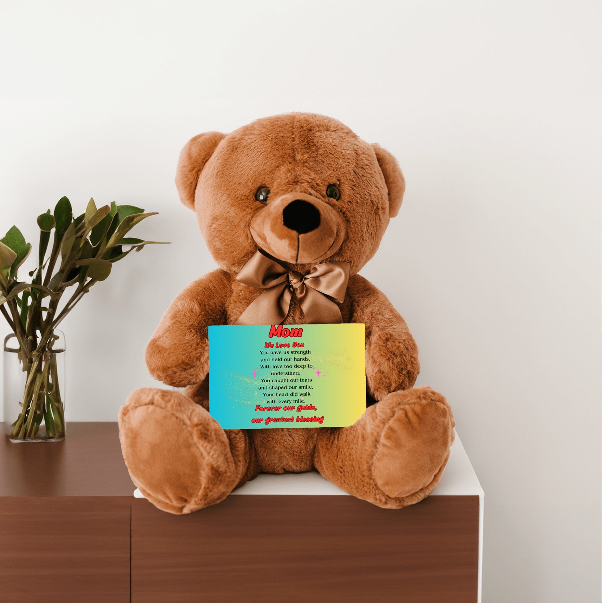 "Plush teddy bear holding a card with the message 'Mom, We Love You – Forever Our Guide' on a pink floral background."