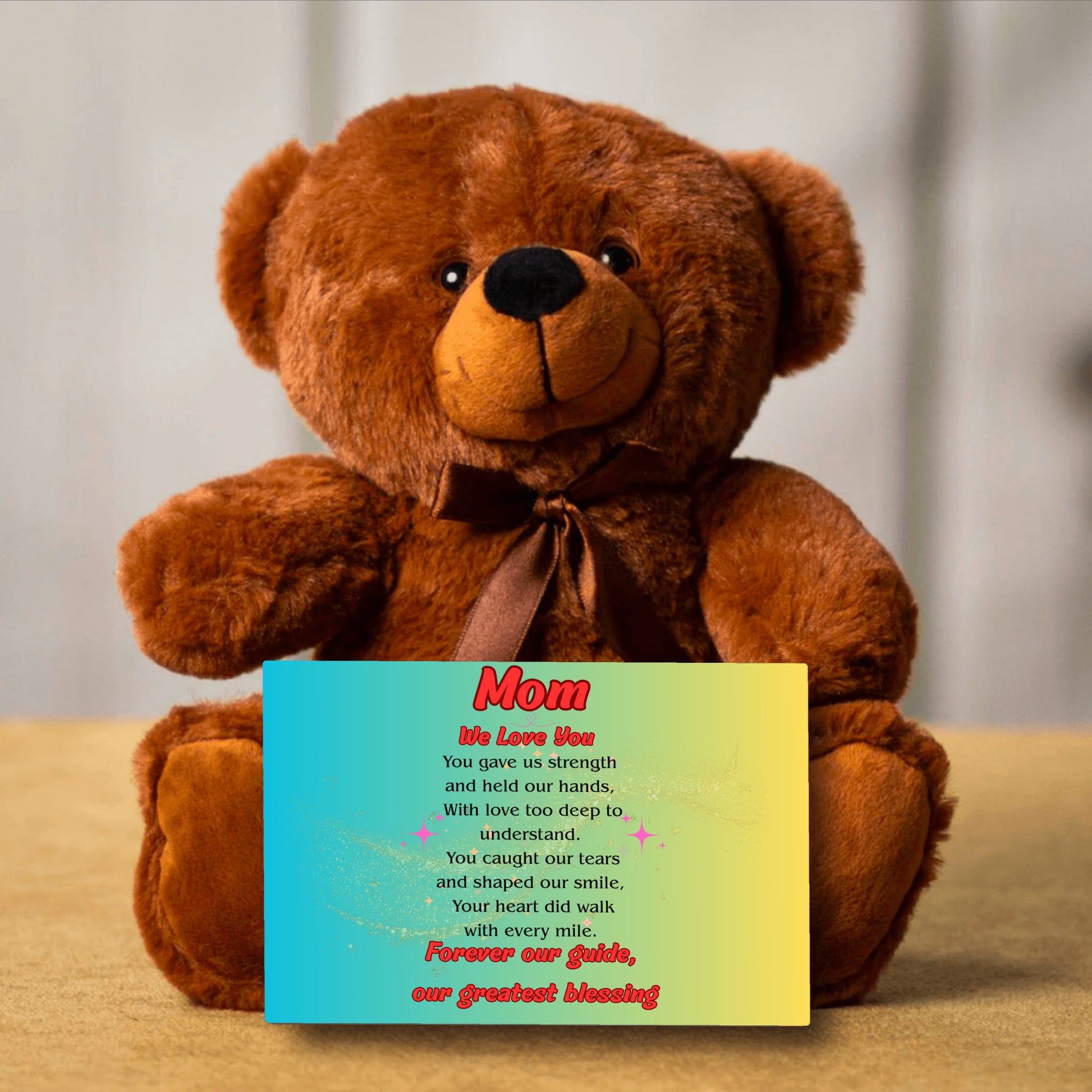 "Plush teddy bear holding a card with the message 'Mom, We Love You – Forever Our Guide' on a pink floral background."