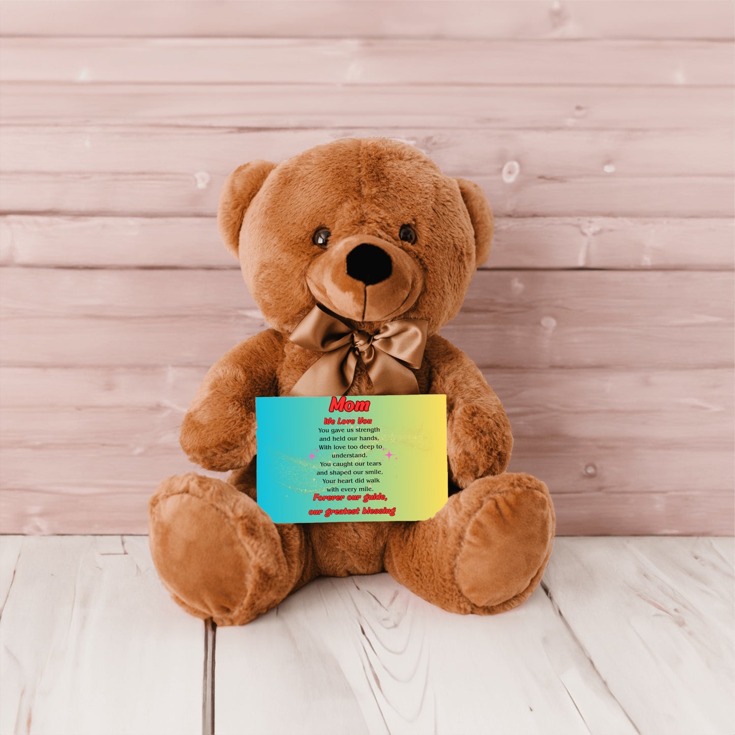 "Plush teddy bear holding a card with the message 'Mom, We Love You – Forever Our Guide' on a pink floral background."