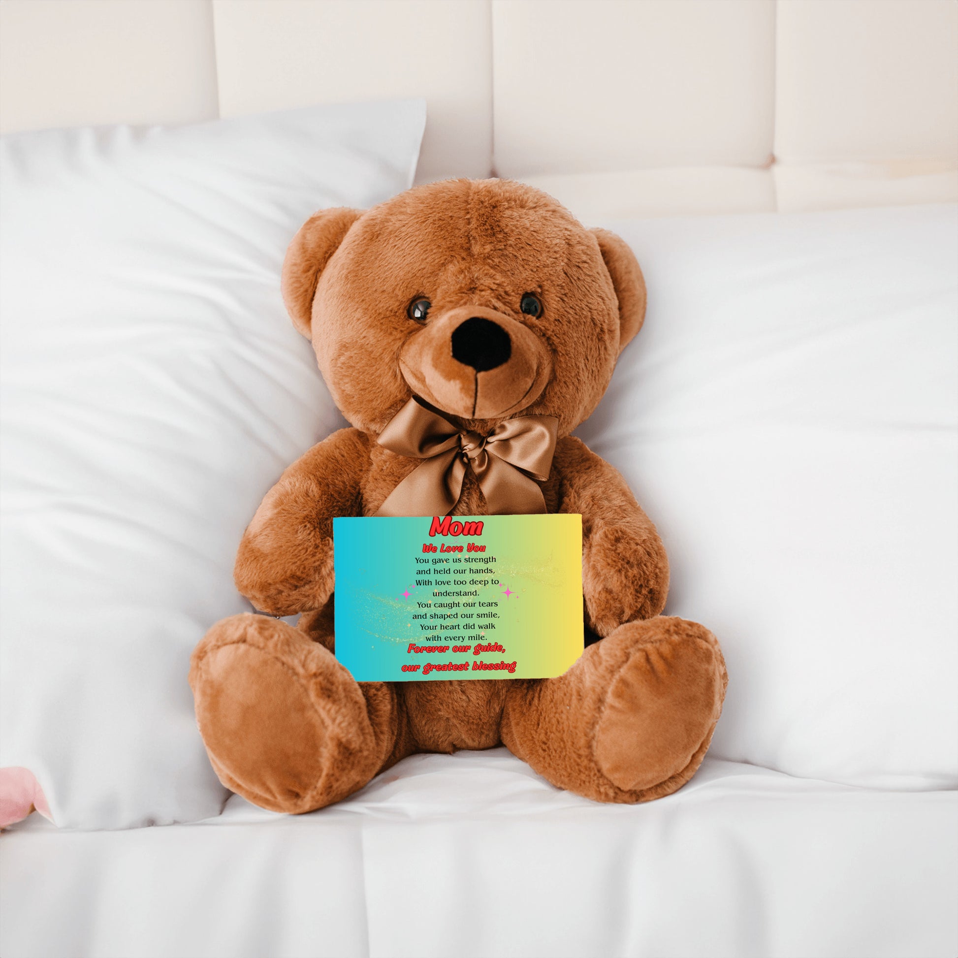 "Plush teddy bear holding a card with the message 'Mom, We Love You – Forever Our Guide' on a pink floral background."
