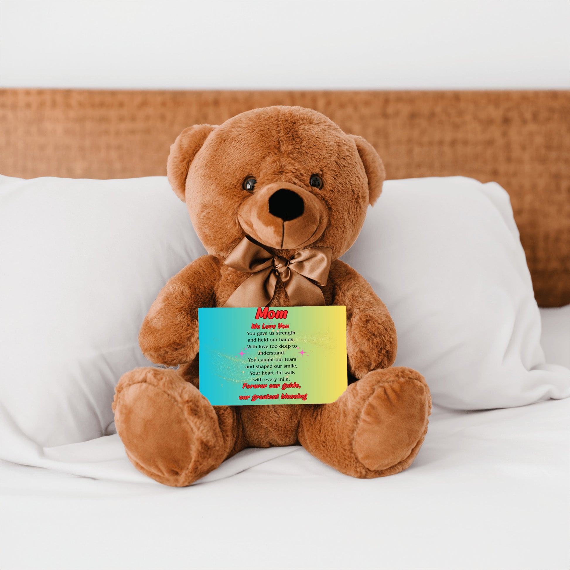 "Plush teddy bear holding a card with the message 'Mom, We Love You – Forever Our Guide' on a pink floral background."