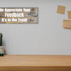 A rectangular wooden plaque featuring the sarcastic phrase "We Appreciate Your Feedback – It’s in the Trash" in bold white and red text on a dark vintage background with ornamental border details.