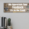 A rectangular wooden plaque featuring the sarcastic phrase "We Appreciate Your Feedback – It’s in the Trash" in bold white and red text on a dark vintage background with ornamental border details.
