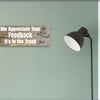 A rectangular wooden plaque featuring the sarcastic phrase "We Appreciate Your Feedback – It’s in the Trash" in bold white and red text on a dark vintage background with ornamental border details.