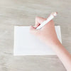 Hand holding a pen over a blank piece of paper on a wooden surface
