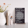 A wood-finish plaque with bold black text that reads “Accept What You Can’t Change” in capital letters, set in a clean and modern font.
