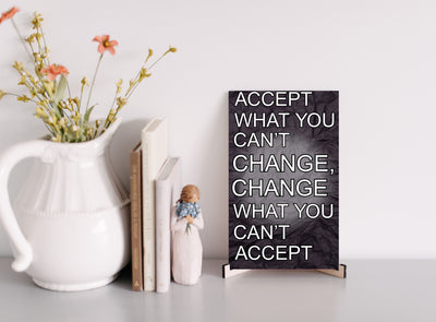 A wood-finish plaque with bold black text that reads “Accept What You Can’t Change” in capital letters, set in a clean and modern font.