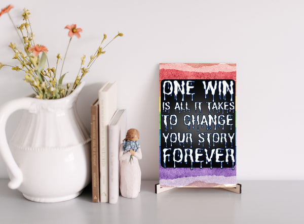 "Motivational wall plaque that reads ‘One Win Is All It Takes to Change Your Story Forever’ displayed above a desk workspace"