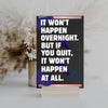 A decorative wood plaque with bold, distressed text reading “It Won’t Happen Overnight,” featuring a minimalist style and comic flair.