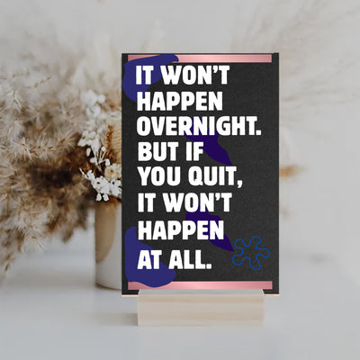 A decorative wood plaque with bold, distressed text reading “It Won’t Happen Overnight,” featuring a minimalist style and comic flair.