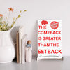 Motivational wall plaque with bold quote: “The Comeback Is Greater Than The Setback” in clean black-and-white print on wood, styled in a home office space.