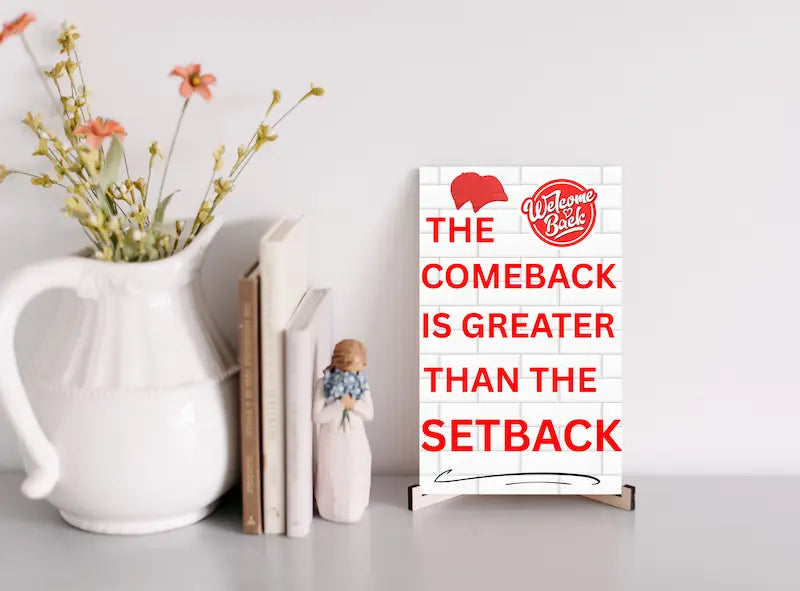 Motivational wall plaque with bold quote: “The Comeback Is Greater Than The Setback” in clean black-and-white print on wood, styled in a home office space.