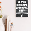 A modern wall plaque that reads “Comfort Is the Enemy of Growth” in bold, minimalist black letters on a clean woodgrain background.