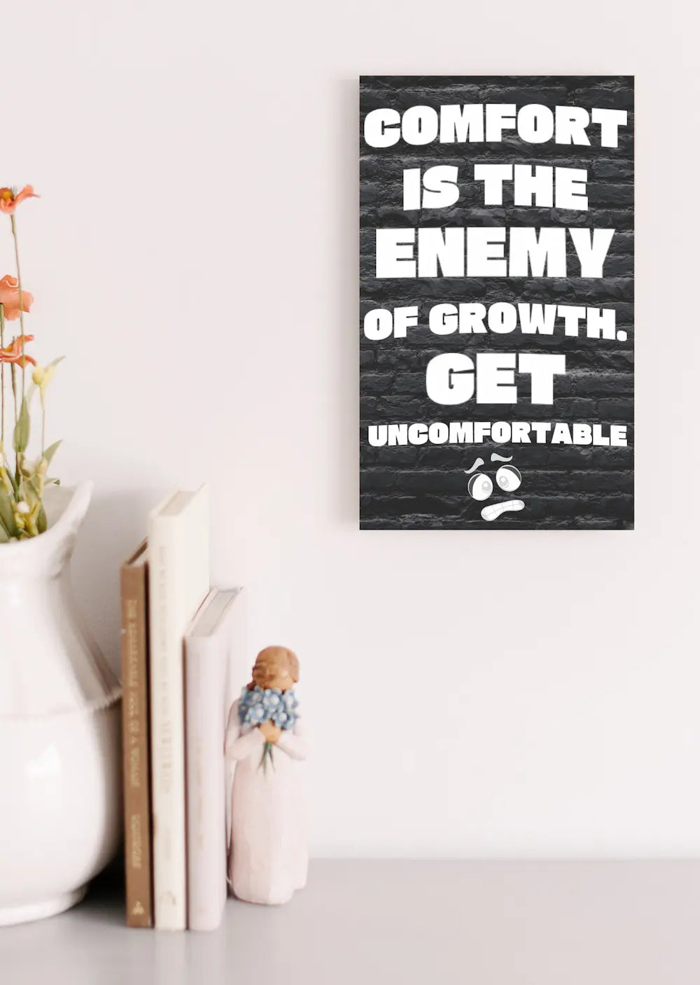 A modern wall plaque that reads “Comfort Is the Enemy of Growth” in bold, minimalist black letters on a clean woodgrain background.