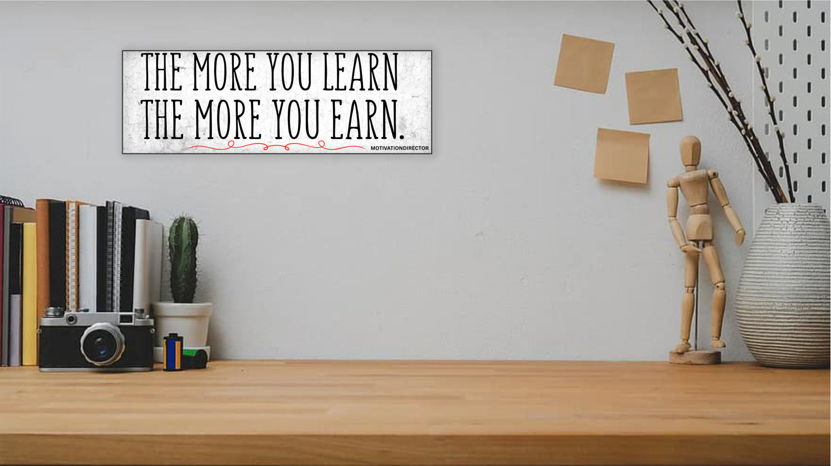 A modern motivational plaque with bold block text that reads “The More You Learn – The More You Earn” on a clean woodgrain background.