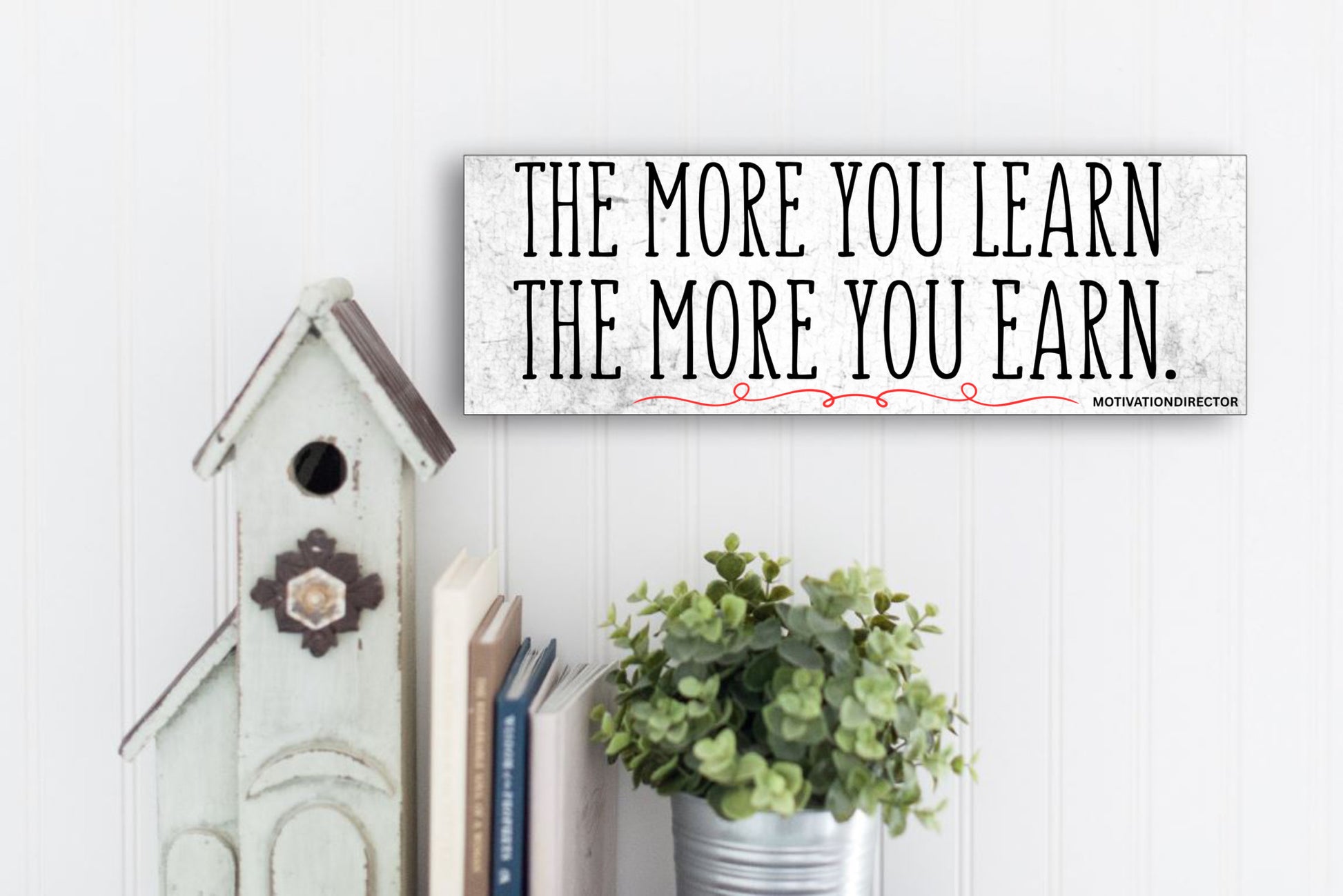 A modern motivational plaque with bold block text that reads “The More You Learn – The More You Earn” on a clean woodgrain background.