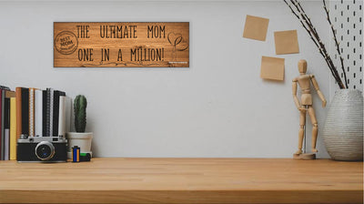 Wooden plaque reading “The Ultimate Mom” in bold script with floral accents and comic-style doodles, perfect for gifting or home décor.