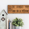 Wooden plaque reading “The Ultimate Mom” in bold script with floral accents and comic-style doodles, perfect for gifting or home décor.