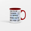 White ceramic mug with black text that reads, “You’re My Favorite Co-Worker (Please Don’t Read Into That).” Set against an office desk with pens and notepads.