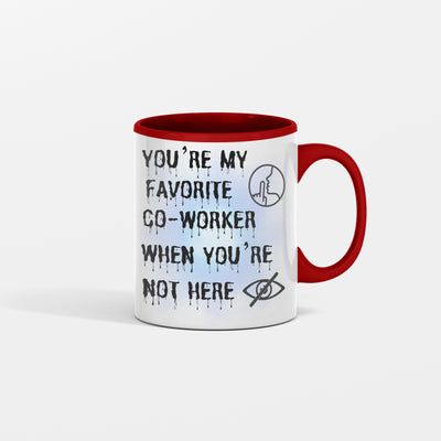 White ceramic mug with black text that reads, “You’re My Favorite Co-Worker (Please Don’t Read Into That).” Set against an office desk with pens and notepads.