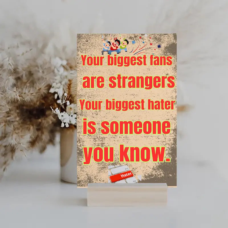 Wooden plaque with bold text: “Your biggest fans are strangers. Your biggest hater is someone you know,” styled with comic-style humor.