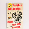 “Funny wall plaque reading 'Slapstick Wake Up Calls Should Come with Warnings' displayed on a kitchen wall near a coffee mug”