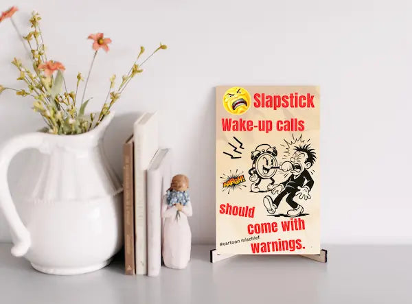 “Funny wall plaque reading 'Slapstick Wake Up Calls Should Come with Warnings' displayed on a kitchen wall near a coffee mug”