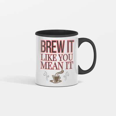 White ceramic coffee mug with bold black text reading "Brew It Like You Mean It" sitting on a wooden desk with steam rising from the cup.