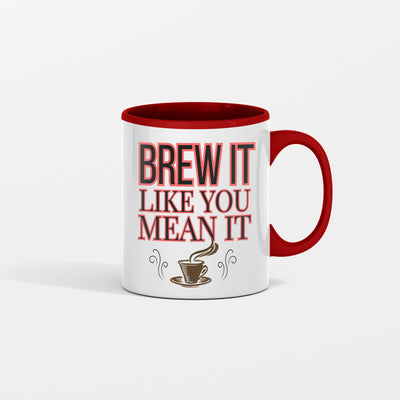 White ceramic coffee mug with bold black text reading "Brew It Like You Mean It" sitting on a wooden desk with steam rising from the cup.