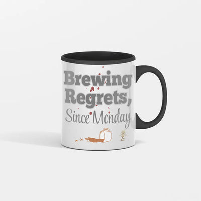 White ceramic mug with bold black text: “Brew Regrets Since Monday” and spilled coffee stain detail on background.