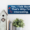 Funny humorous wall plaque with the phrase “YES, I TALK BACK – THAT’S WHY I’M INTERESTING” in bold lettering.