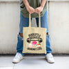“Beige tote bag with design featuring a barbell, pink frosted donut, cupcake, and fruit cheesecake with the humorous phrase ‘Deadlifts & Desserts Grandma’s Lifes.’”