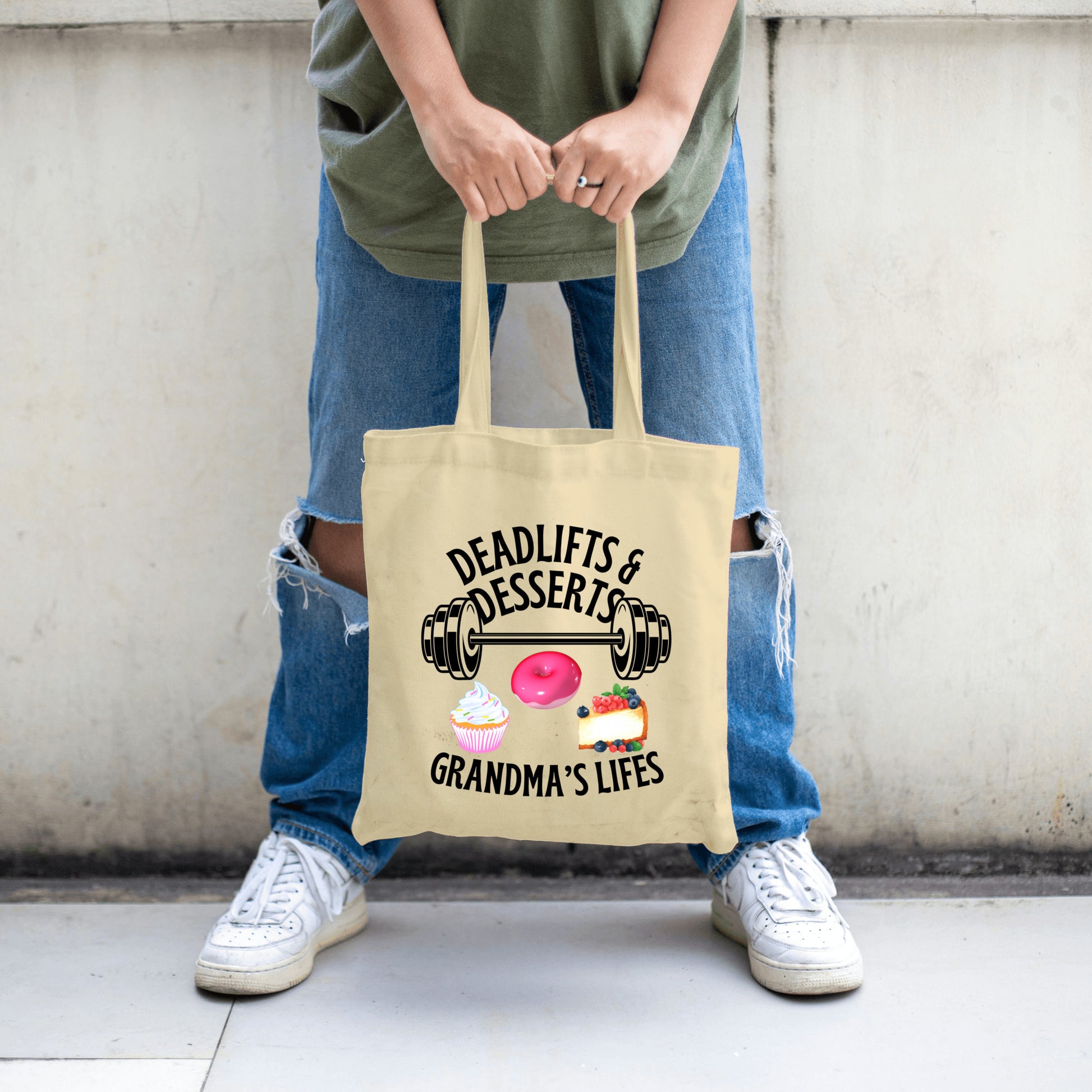 “Beige tote bag with design featuring a barbell, pink frosted donut, cupcake, and fruit cheesecake with the humorous phrase ‘Deadlifts & Desserts Grandma’s Lifes.’”
