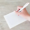Hand holding a white pen over a white sheet of paper on a light wooden surface