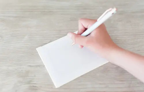 Hand holding a white pen over a white sheet of paper on a light wooden surface