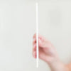 Hand holding a white straw against a plain background