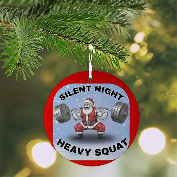 Christmas ornament with Santa Claus lifting weights and 'Silent Night Heavy Squat' text, hanging on a tree.
